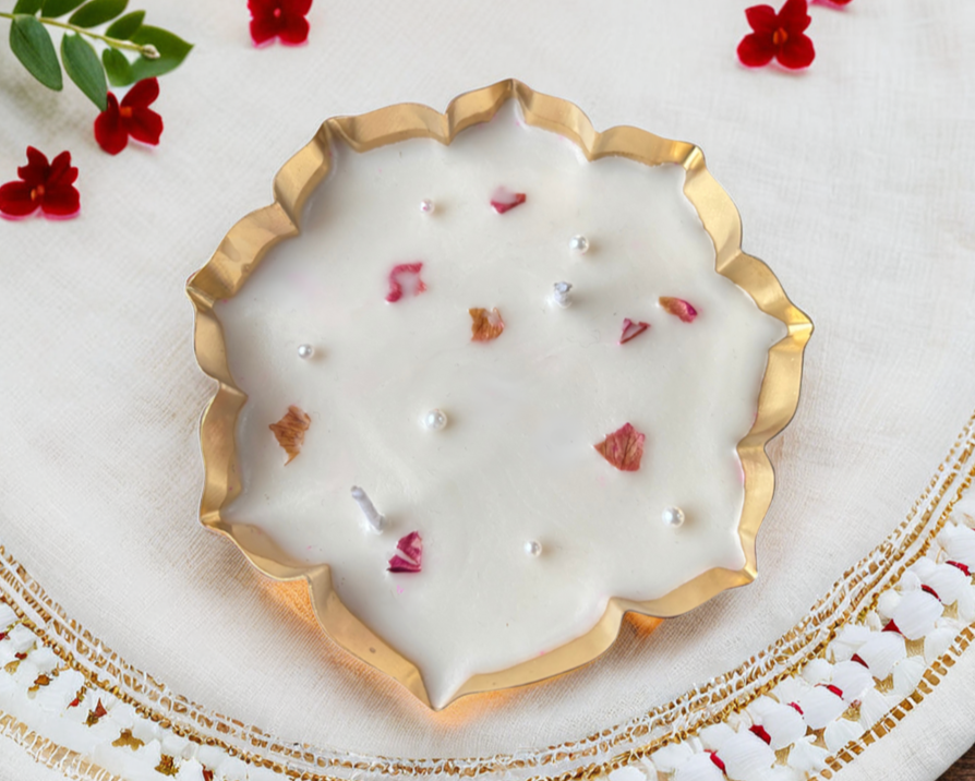 Decorative candle with gold rim on a white plate with red flowers and green leaves.