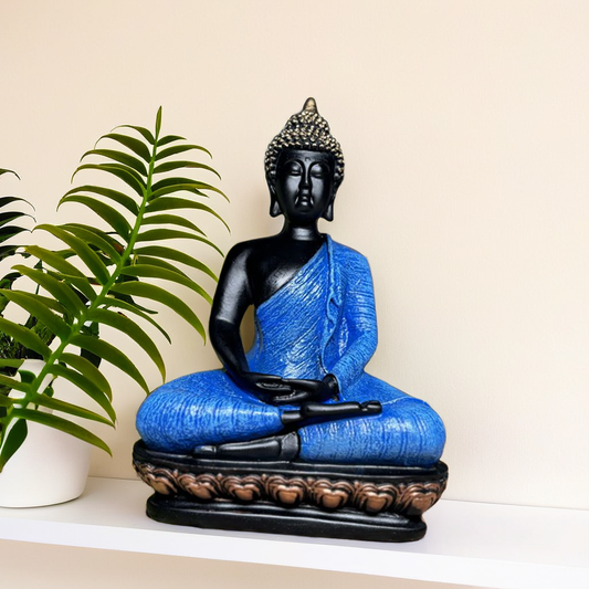 Buddha statue with blue robe and black hair on a white surface with a plant in the background