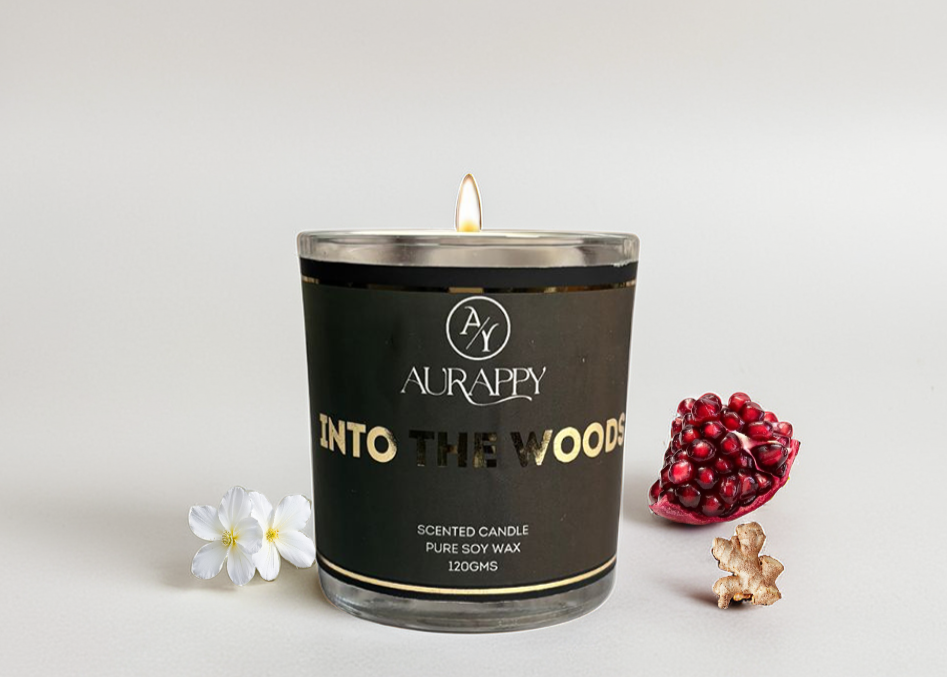Aurappy candle labeled 'Into The Woods' with pomegranate, jasmine, and ginger elements on a light background