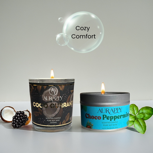 Two scented candles with labels 'Coco Currant' and 'Choco Peppermint' on a white surface, with a bubble labeled 'Cozy Comfort' in the background.
