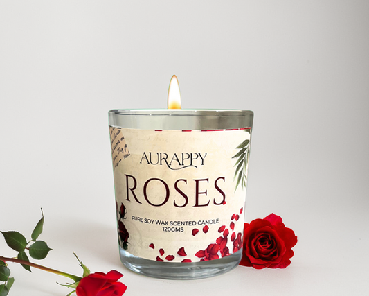 Aurappy 'Roses' scented candle with a lit wick on a white background, surrounded by red roses.